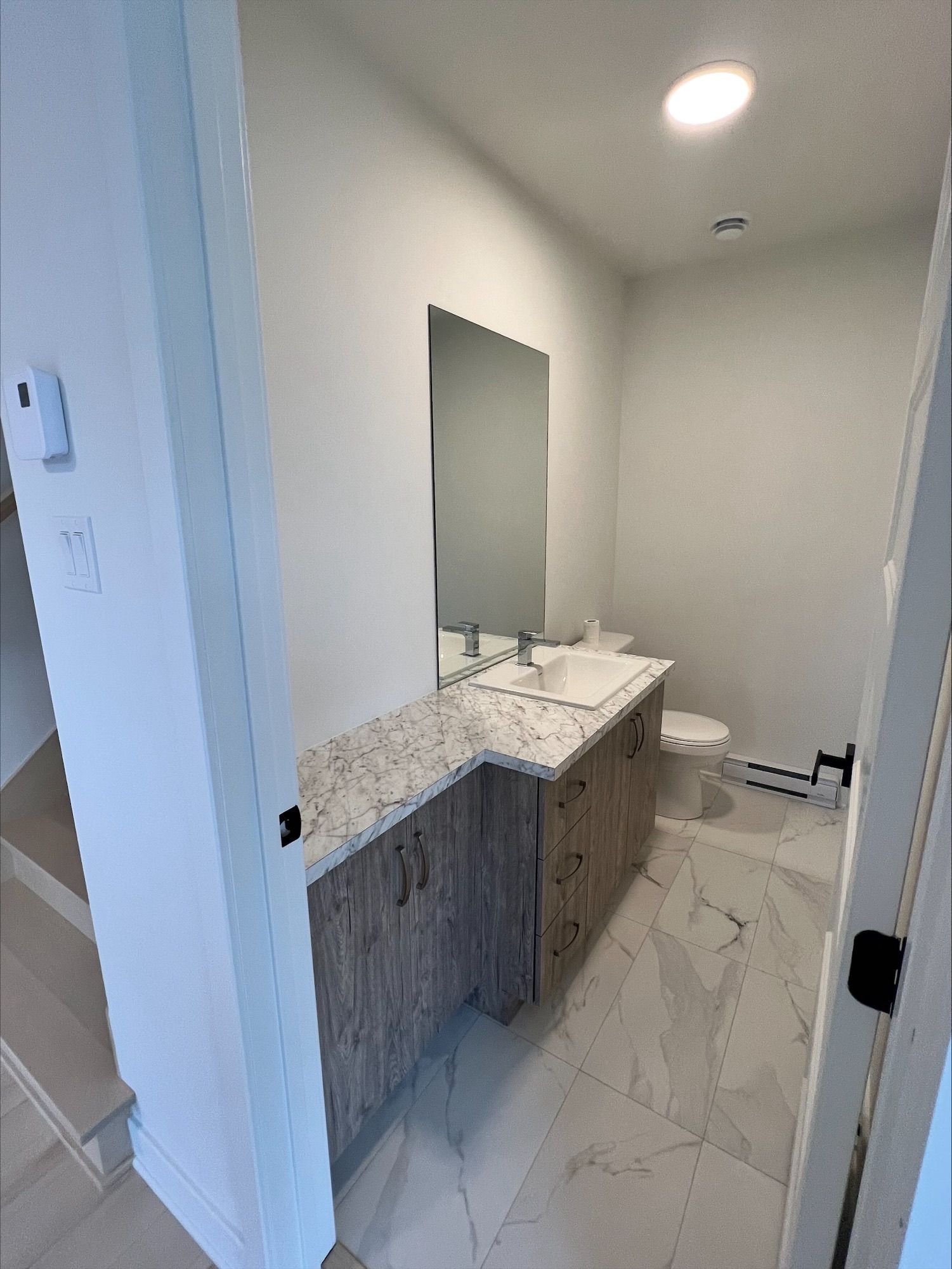 Une petite salle de bain moderne avec une vanité, des toilettes et un grand miroir; tons gris clair et blanc.