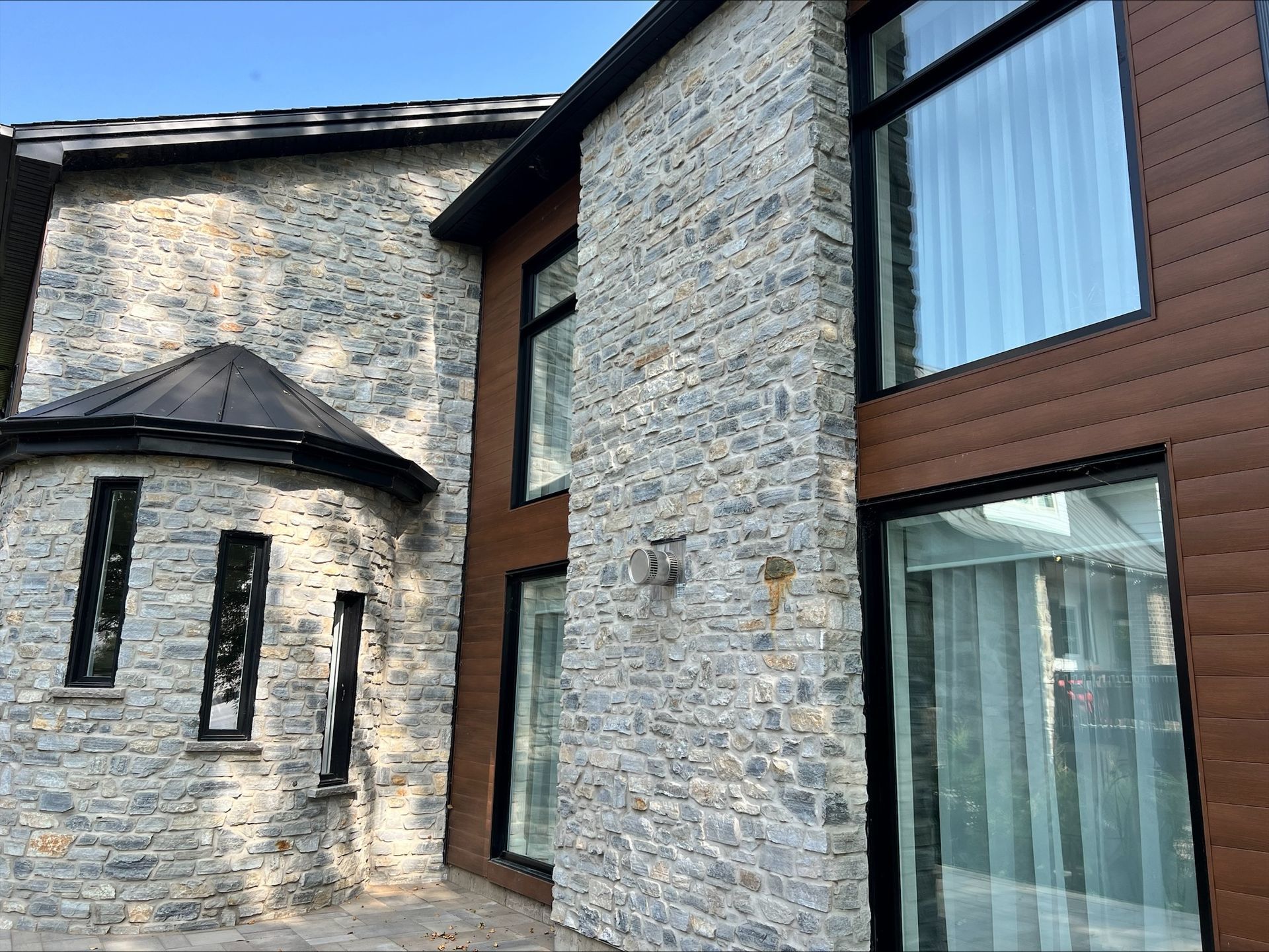 Extérieur de maison moderne avec revêtement en pierre et en bois, grandes fenêtres et garnitures noires.