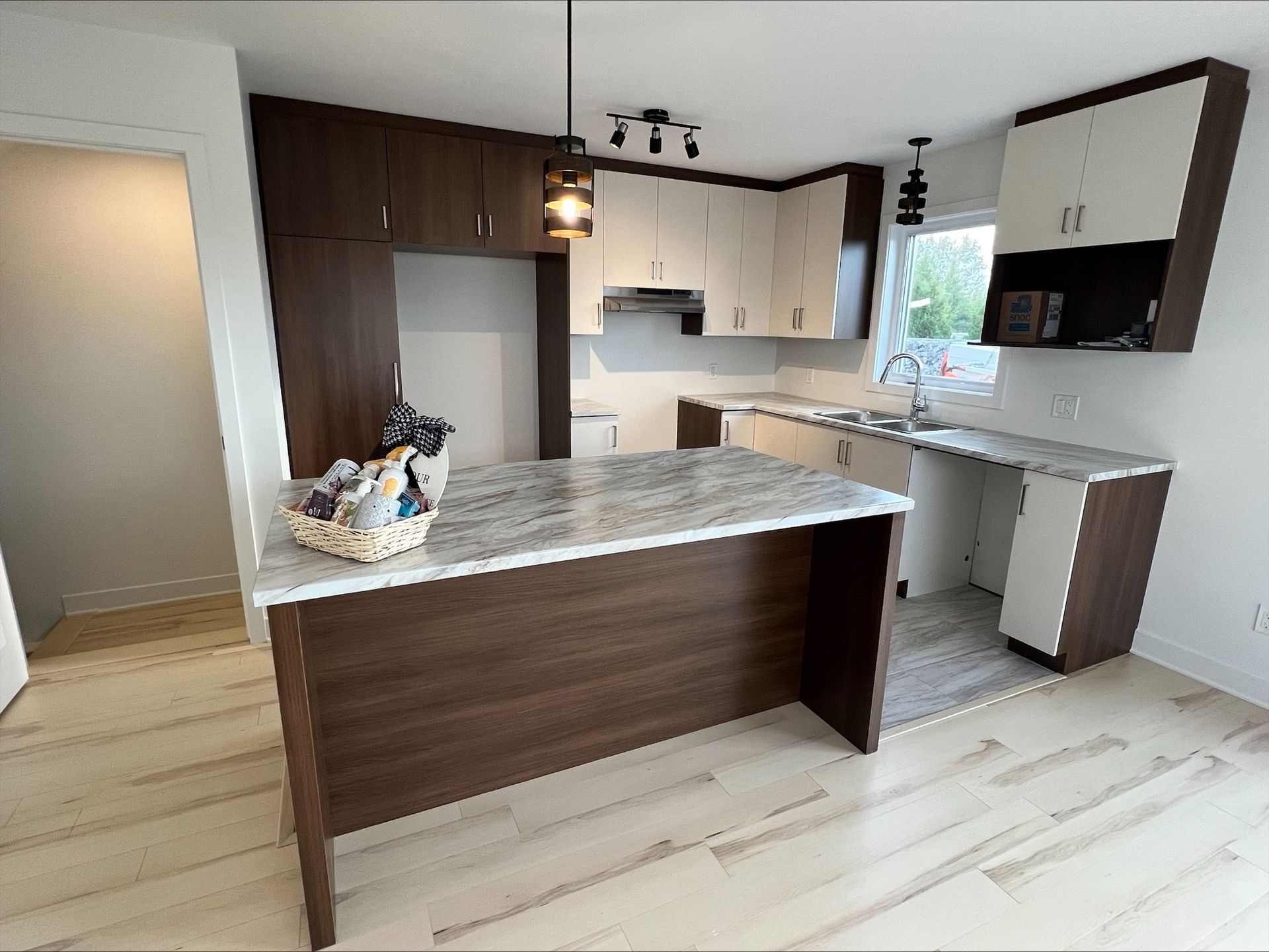 Cuisine moderne avec armoires marron foncé et crème, un îlot de comptoir en granit et un parquet en bois clair.