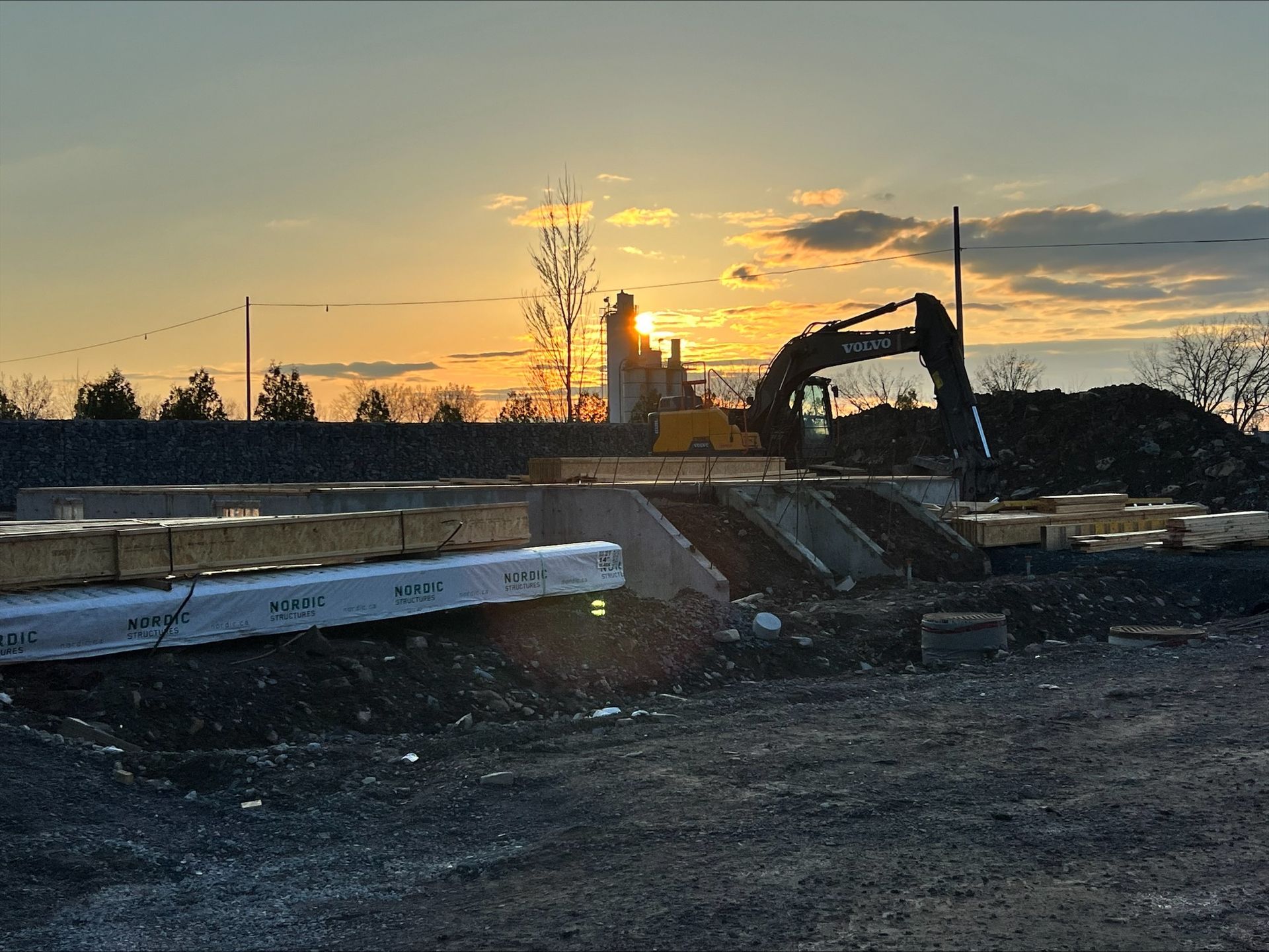 Chantier de construction au coucher du soleil : excavatrice et matériaux de construction se découpant sur le soleil couchant.