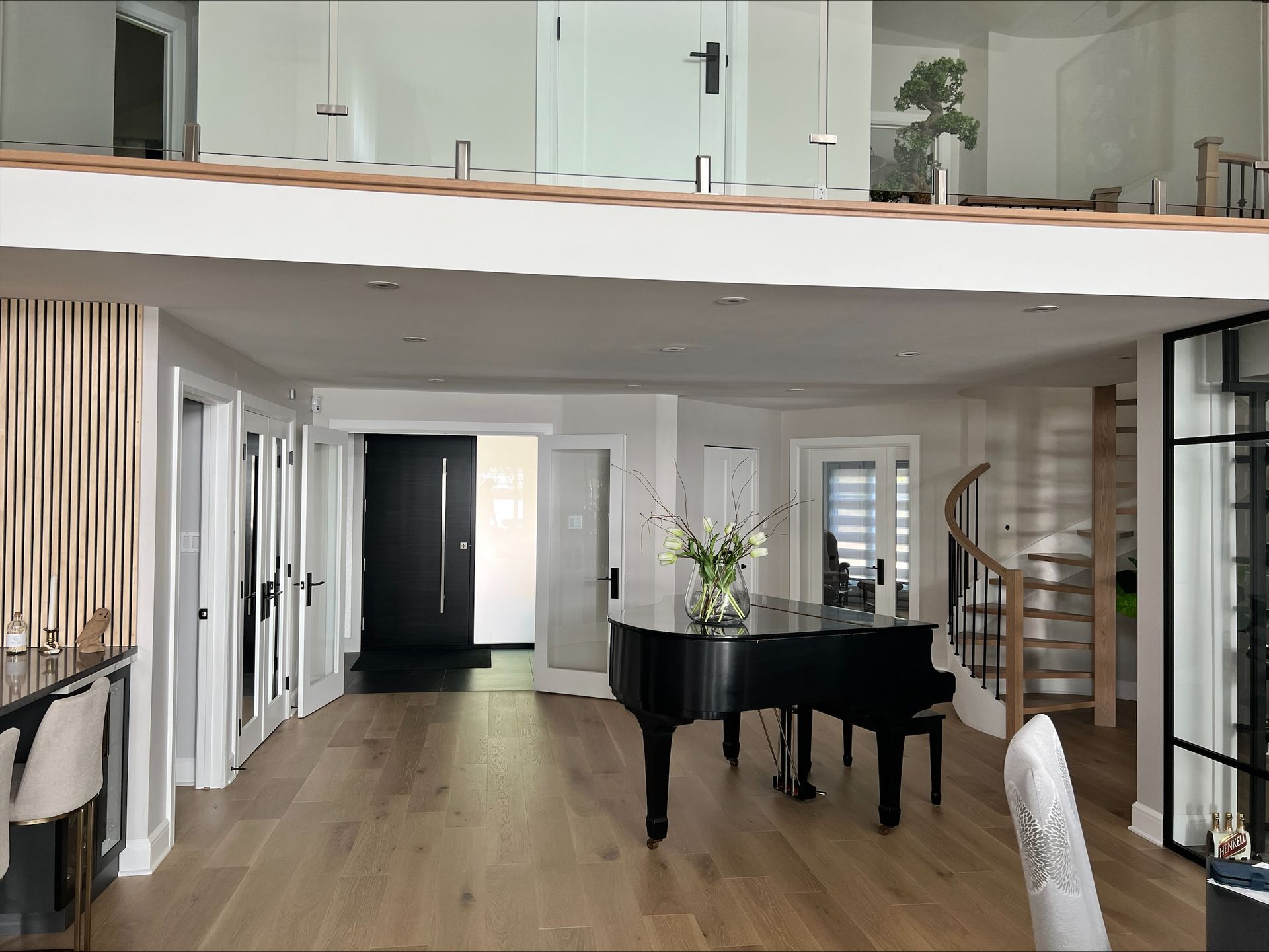 Un grand espace de vie avec un piano à queue noir comme point central, des planchers en bois clair et un loft avec rampe en verre au-dessus.