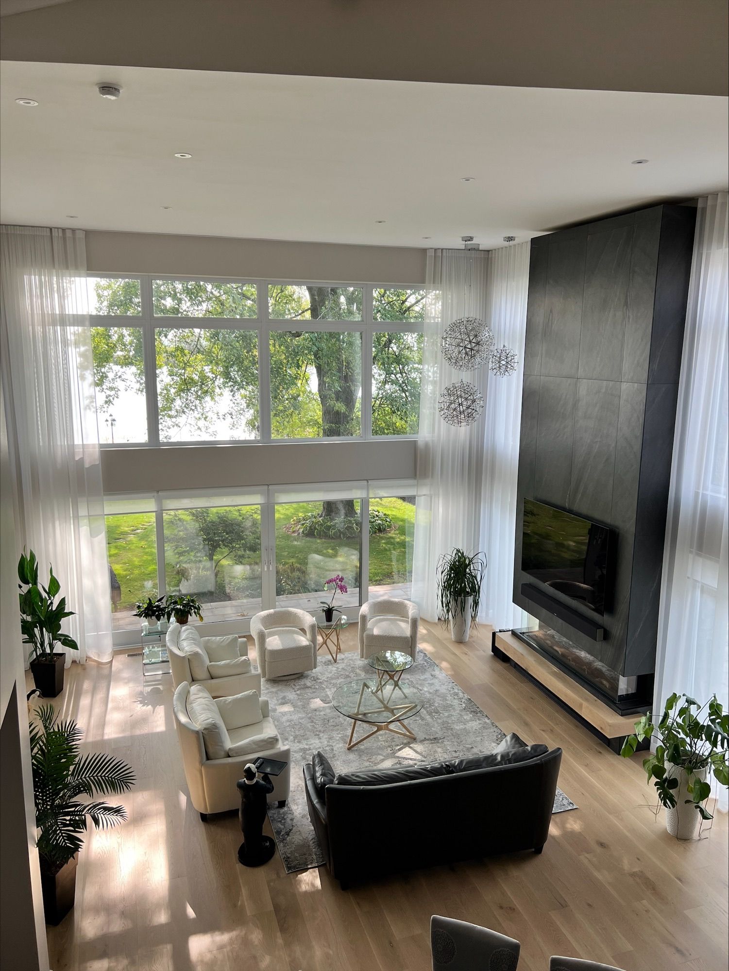 Vue en plongée d'un salon moderne avec des baies vitrées, des meubles blancs et une cheminée noire.