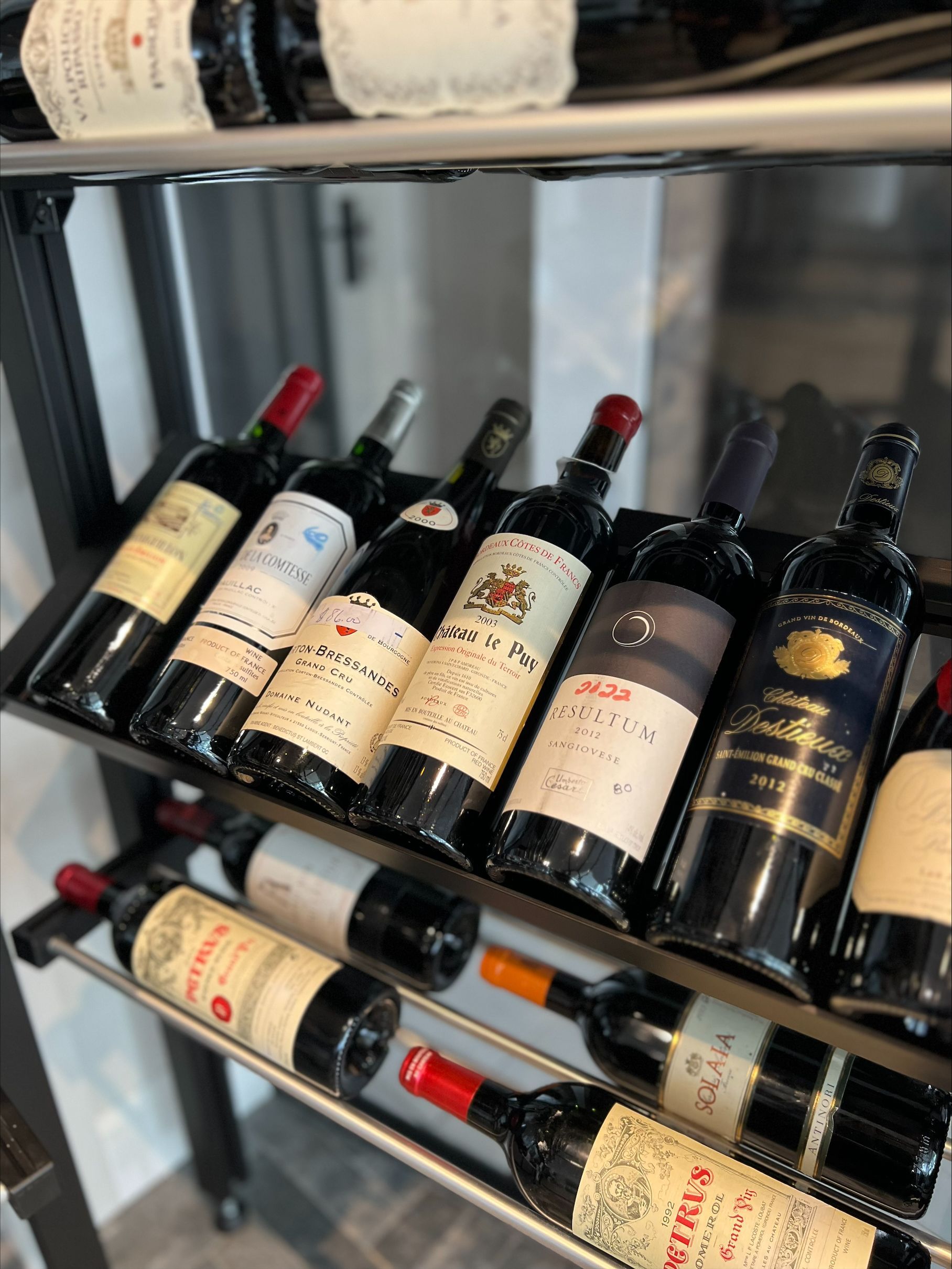 Un casier à vin contenant diverses bouteilles de vin rouge. Les bouteilles sont disposées sur des étagères, étiquettes visibles, mettant en valeur une collection.