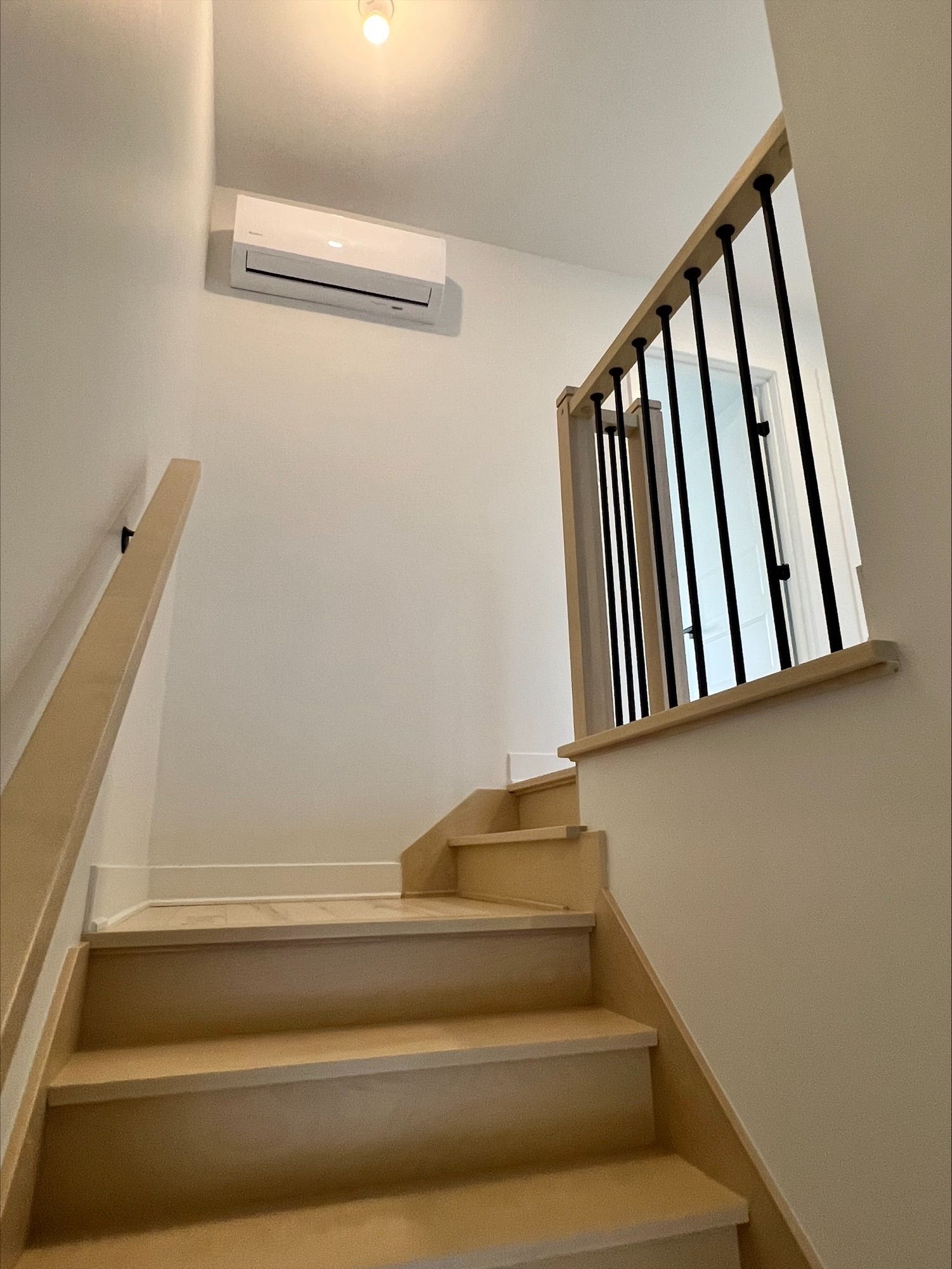 Un escalier avec marches en bois et rampe mène à l'étage. Un climatiseur est fixé au mur.