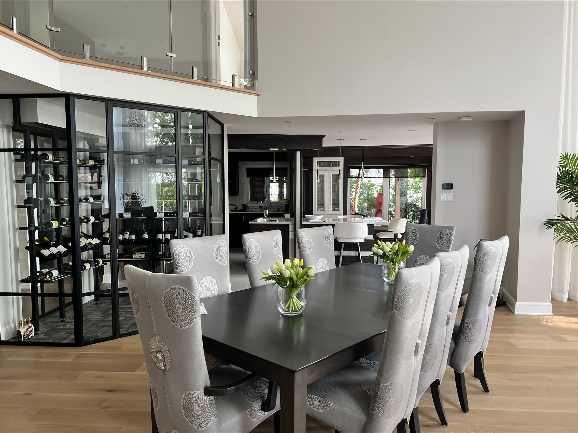 Élégante salle à manger avec table en bois foncé, chaises ornées et casier à vin vitré. Parquet clair et vue sur la cuisine.