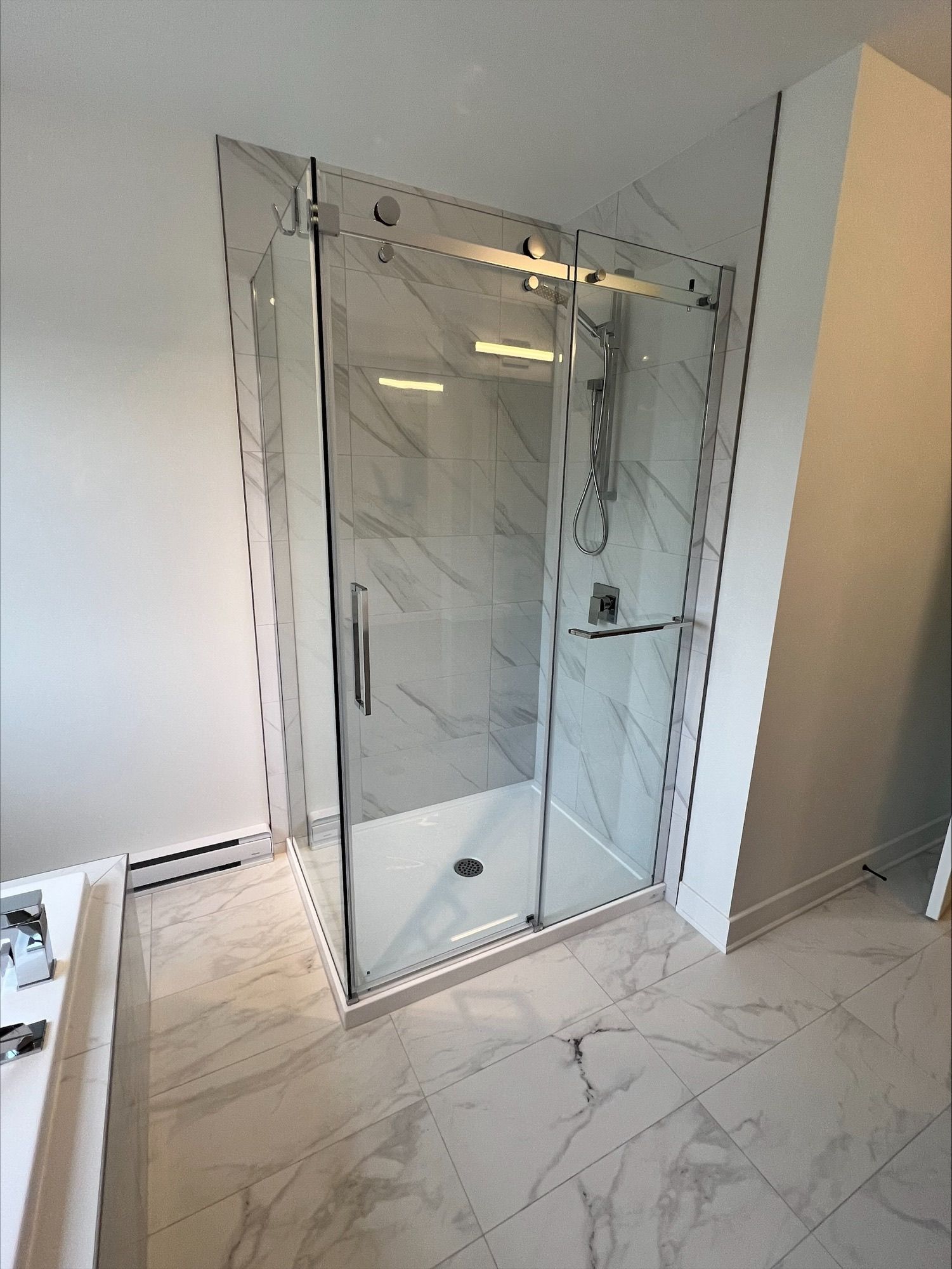 Une douche moderne en verre avec un carrelage imitation marbre dans une salle de bain.