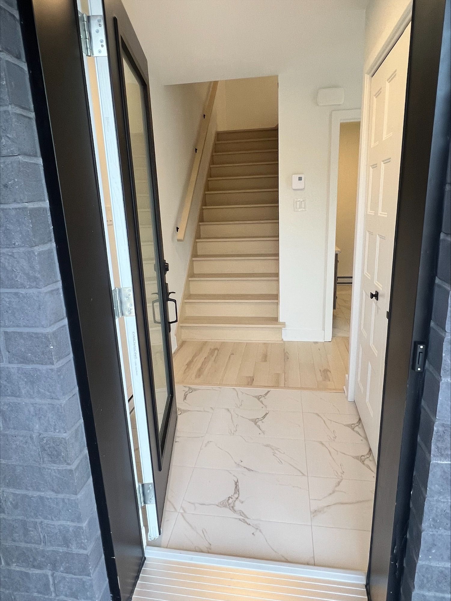 Une porte d'entrée menant à une maison avec un escalier et une porte fermée. Sol et murs de couleur claire.