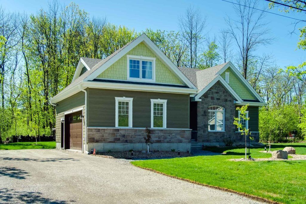 Une maison verte avec une façade en pierre, un toit vert clair et une allée par une journée ensoleillée.