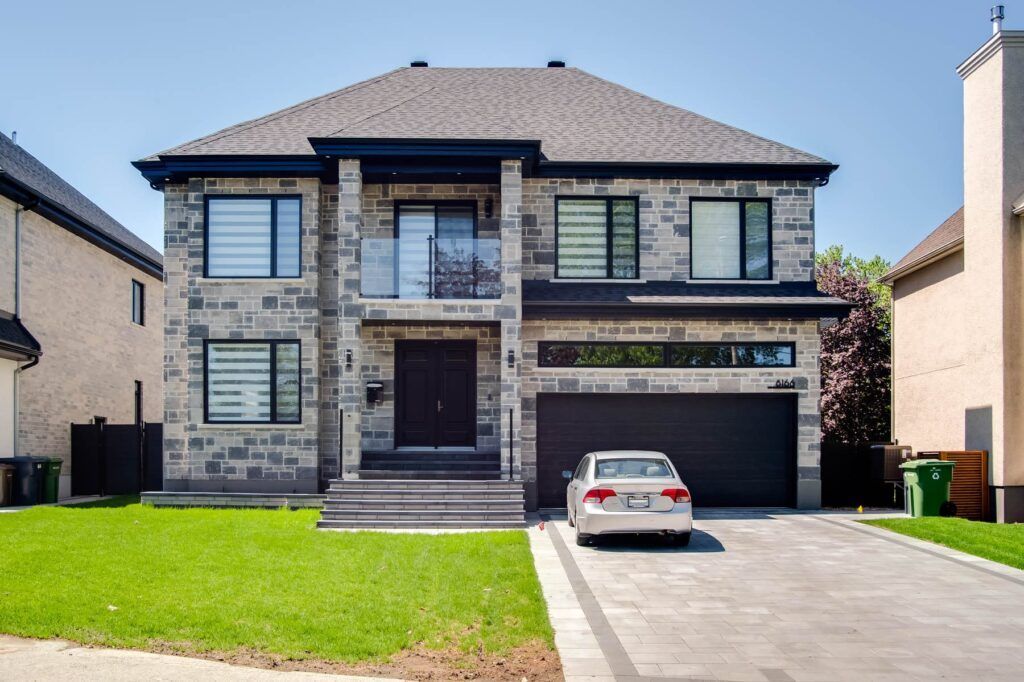 Une maison en pierre à deux étages avec une voiture garée dans l'allée par une journée ensoleillée. La pelouse est verte.