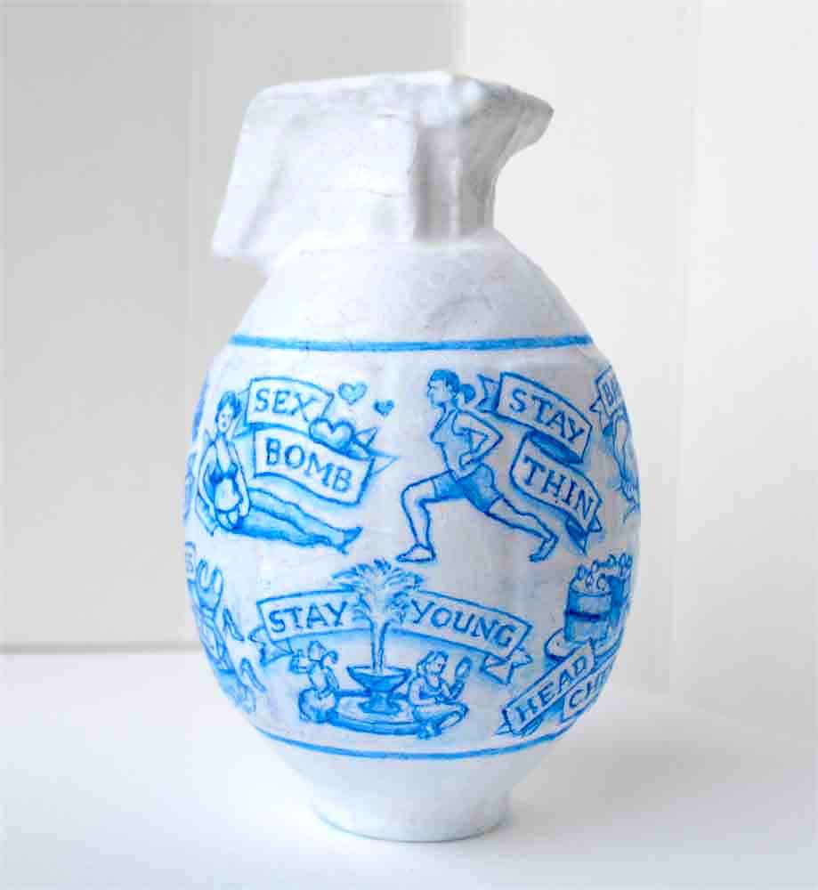 Close up of a hand-painted artwork of a grenade covered in images  depicting the pressures modern society puts on women.