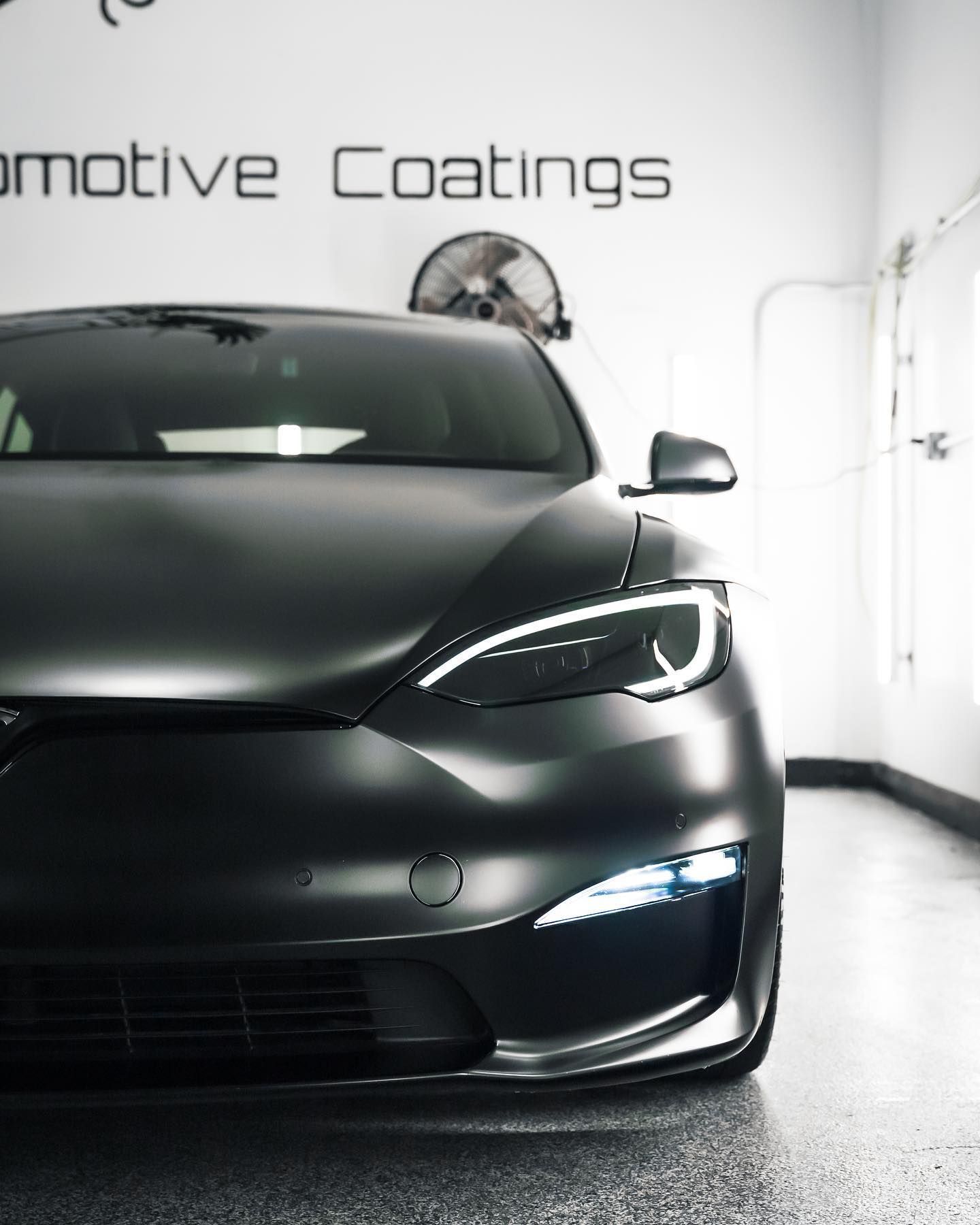 A black car is parked in front of a sign that says automotive coatings