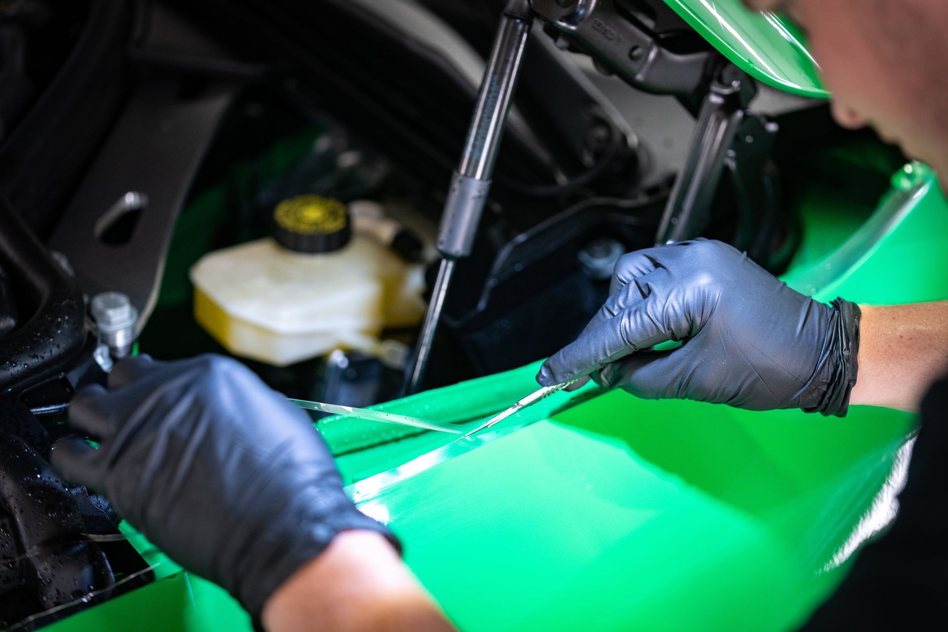A person wearing black gloves is working on a green car.