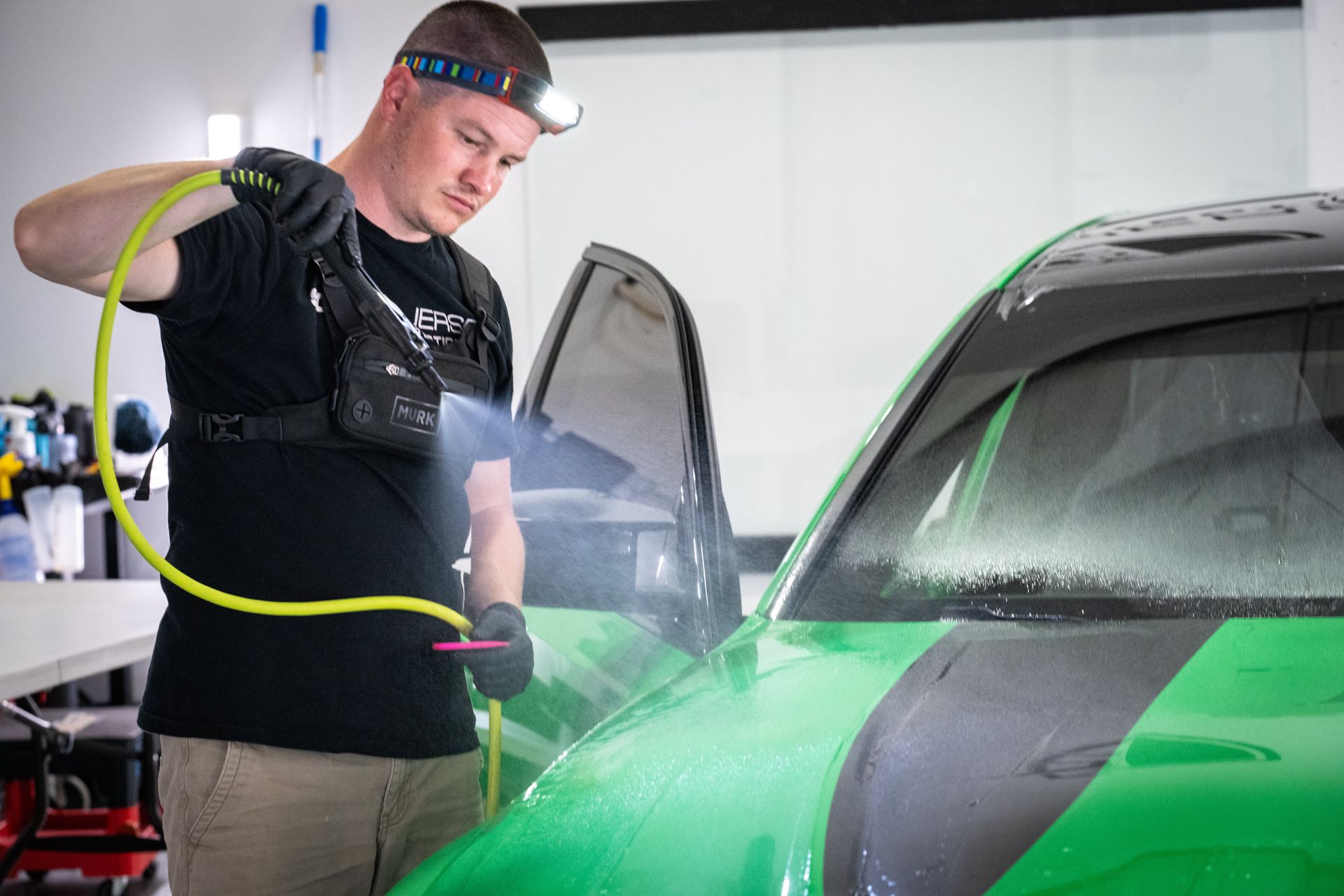 A man is cleaning a green car with a spray bottle.