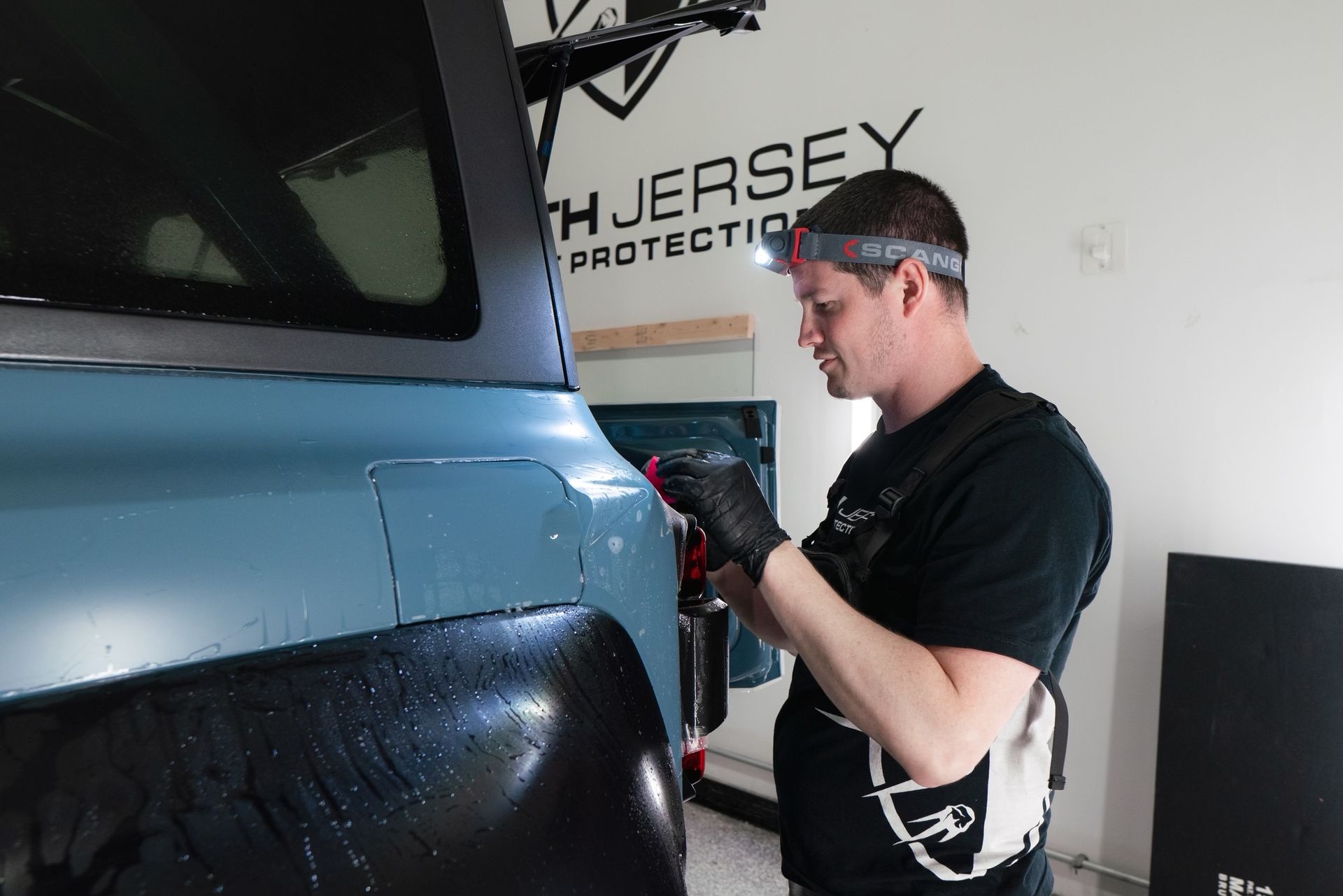 A man is working on a car in front of a wall that says jersey protection