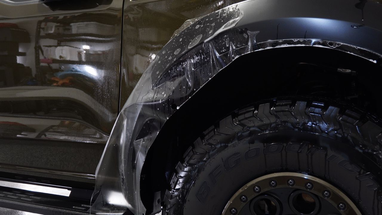 A close up of a car fender with a protective film on it.