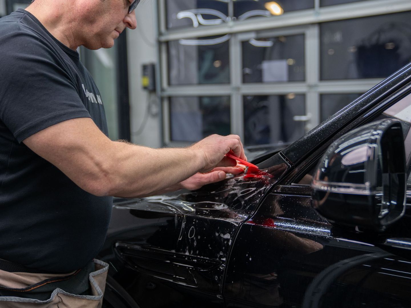 A man is working on a black car in a garage.