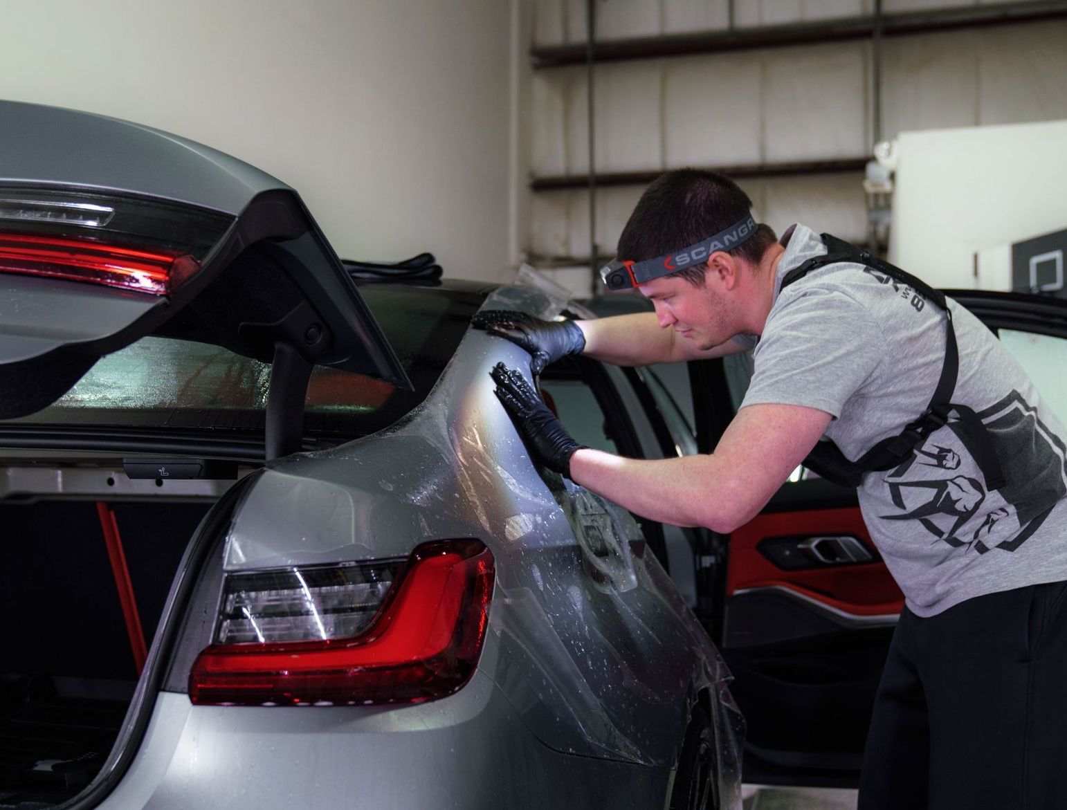 A man is wrapping a car with plastic wrap in a garage.