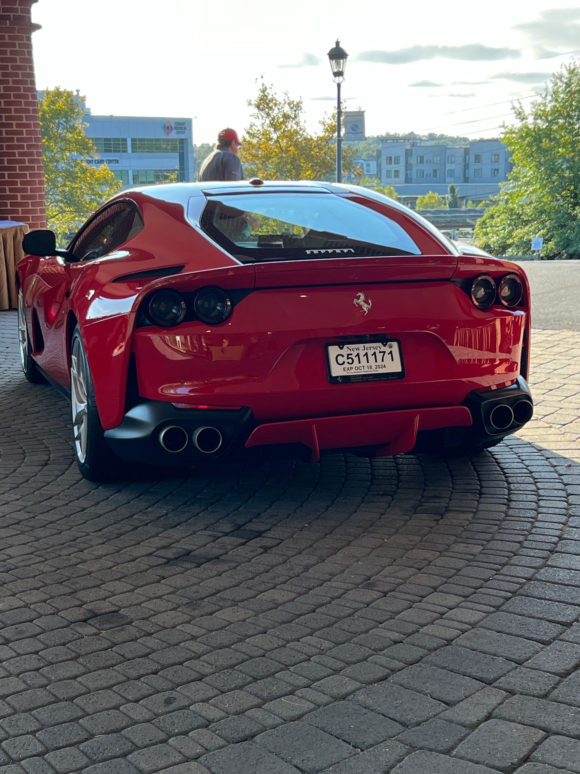 A red ferrari is parked on a brick sidewalk.
