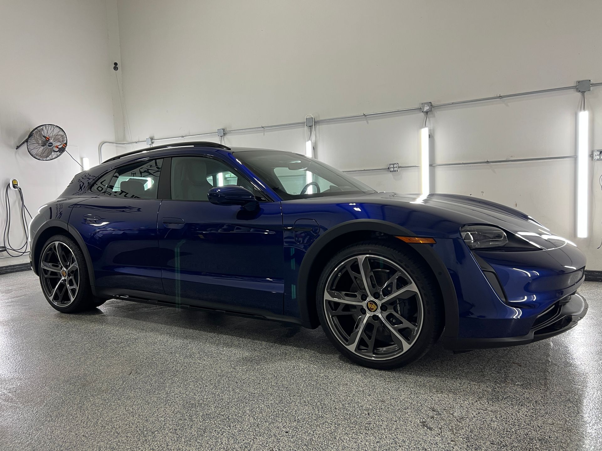 A blue porsche taycan turbo s is parked in a garage.
