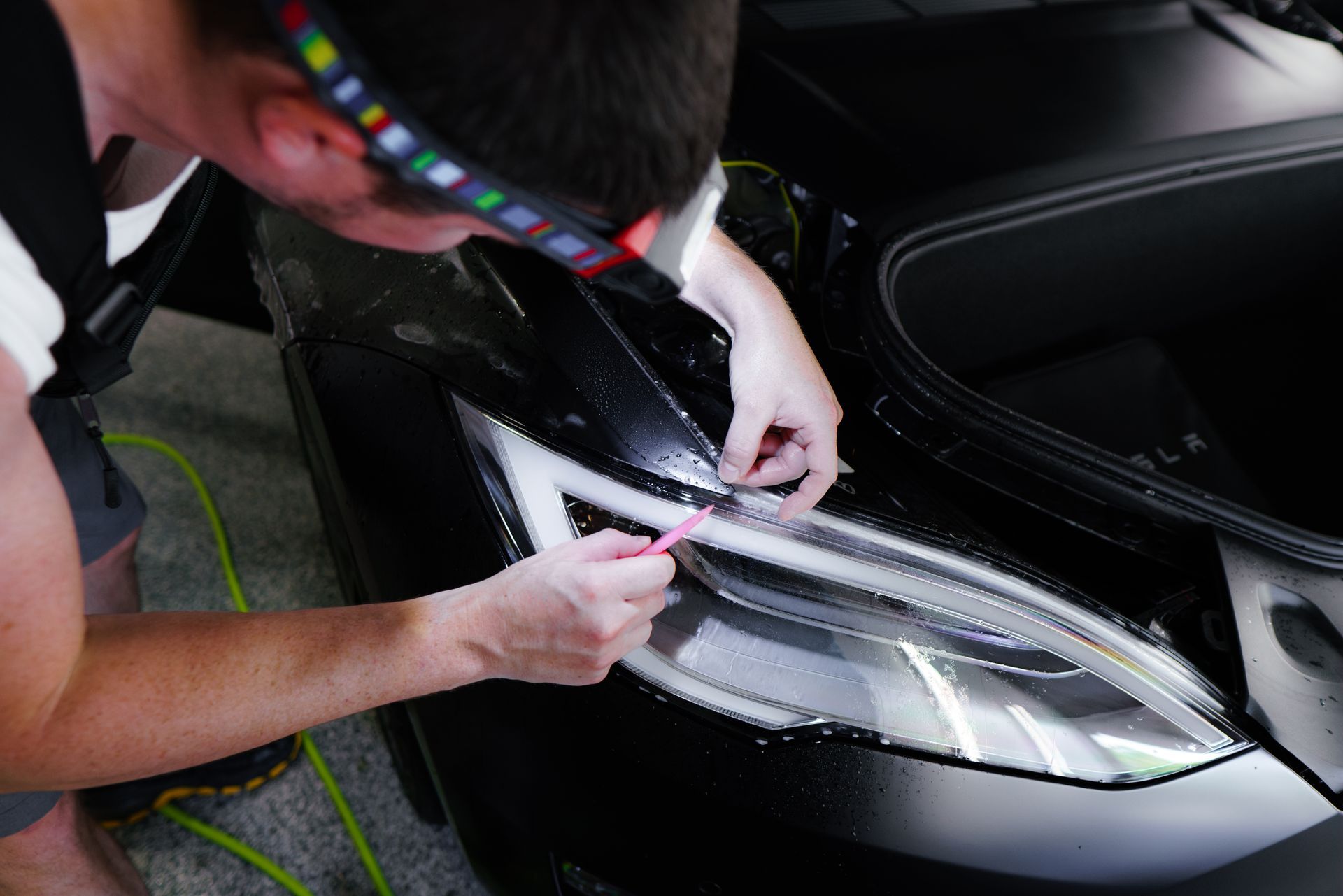 A man is applying a protective film to the headlight of a car.