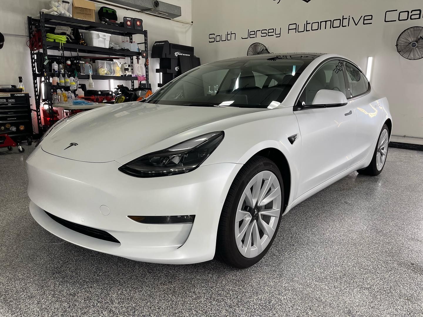 A white tesla model 3 is parked in a garage.