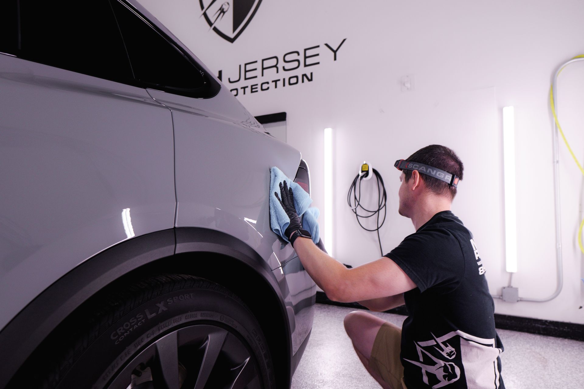 A man is cleaning a car with a cloth in a garage.