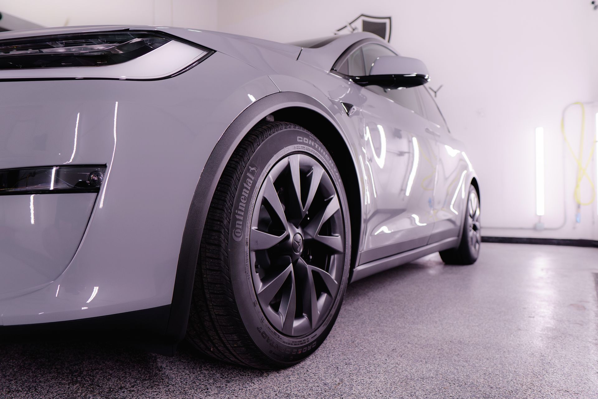 A gray tesla model s is parked in a garage.