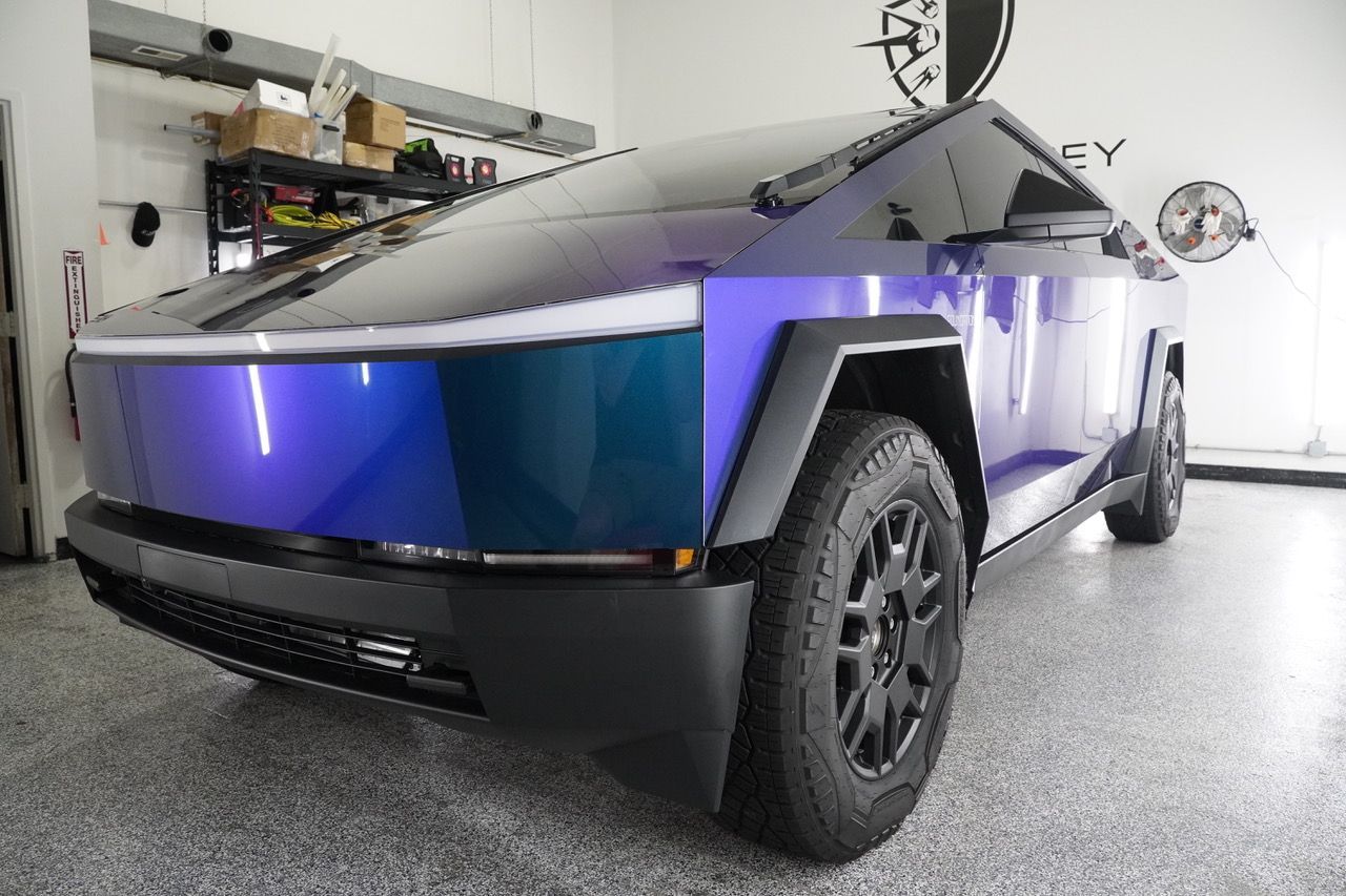 A purple and black tesla cybertruck is parked in a garage.