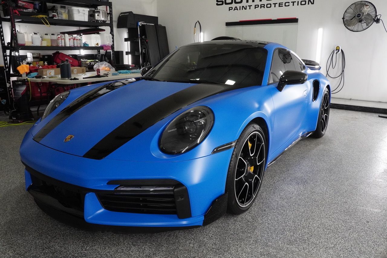 A blue sports car with black stripes is parked in a garage.