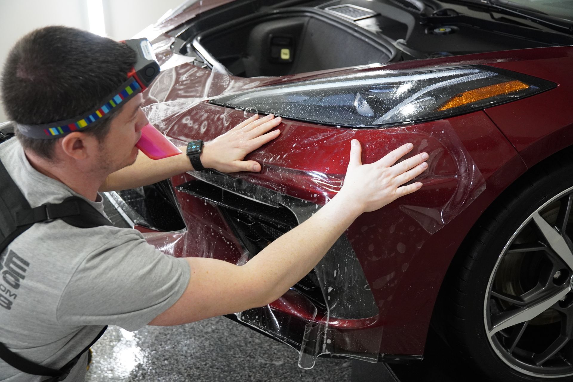 A man is applying protective film to the front of a red car.