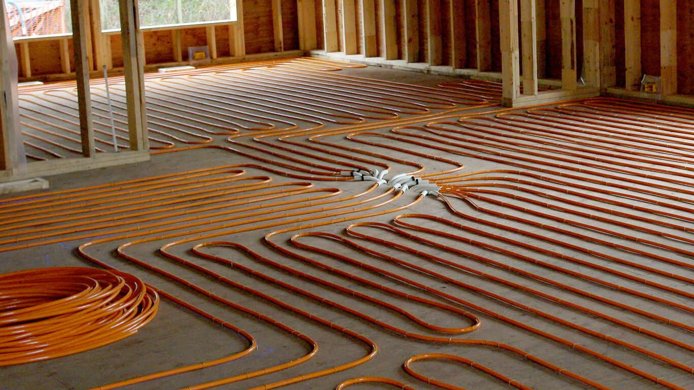 Orange radiant floor heating tubes laid on concrete floor in a house under construction.