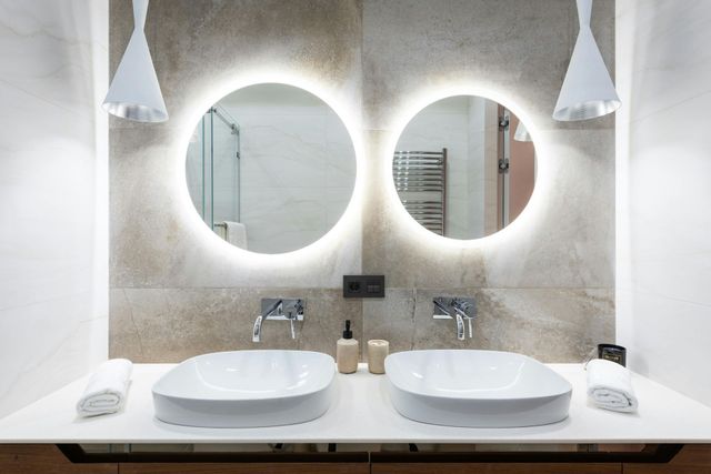Modern bathroom with two sinks, round mirrors with lights, and white pendant lamps.