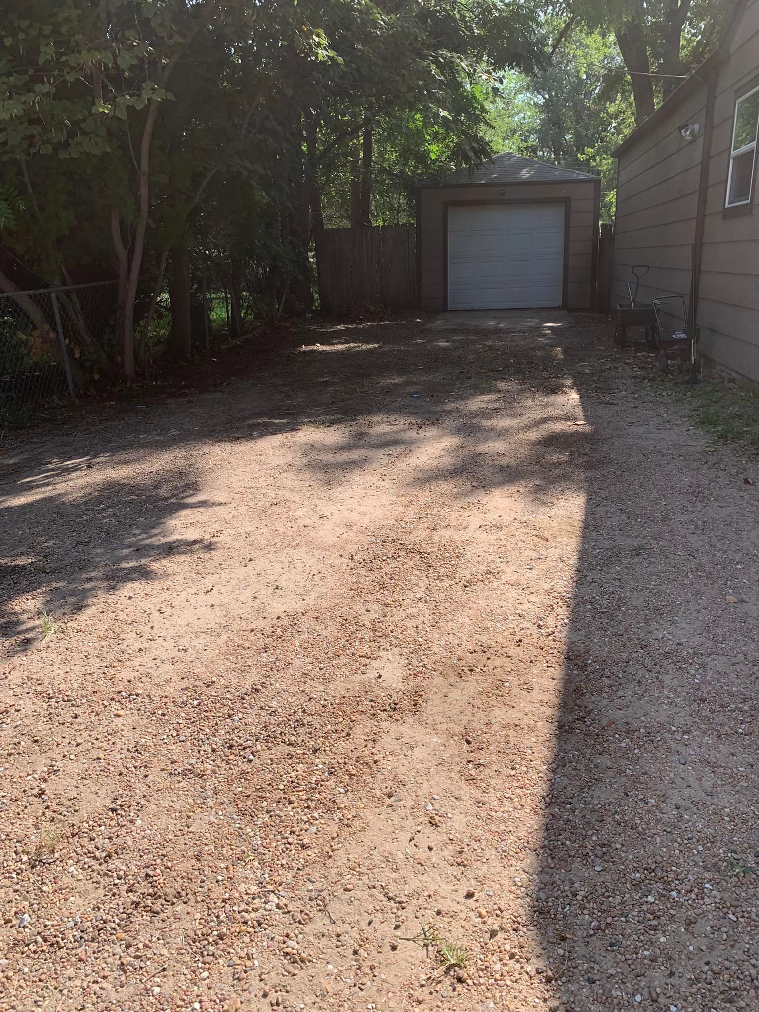 Gravel driveway leading to a garage, trees on the left and a house on the right, sunny.