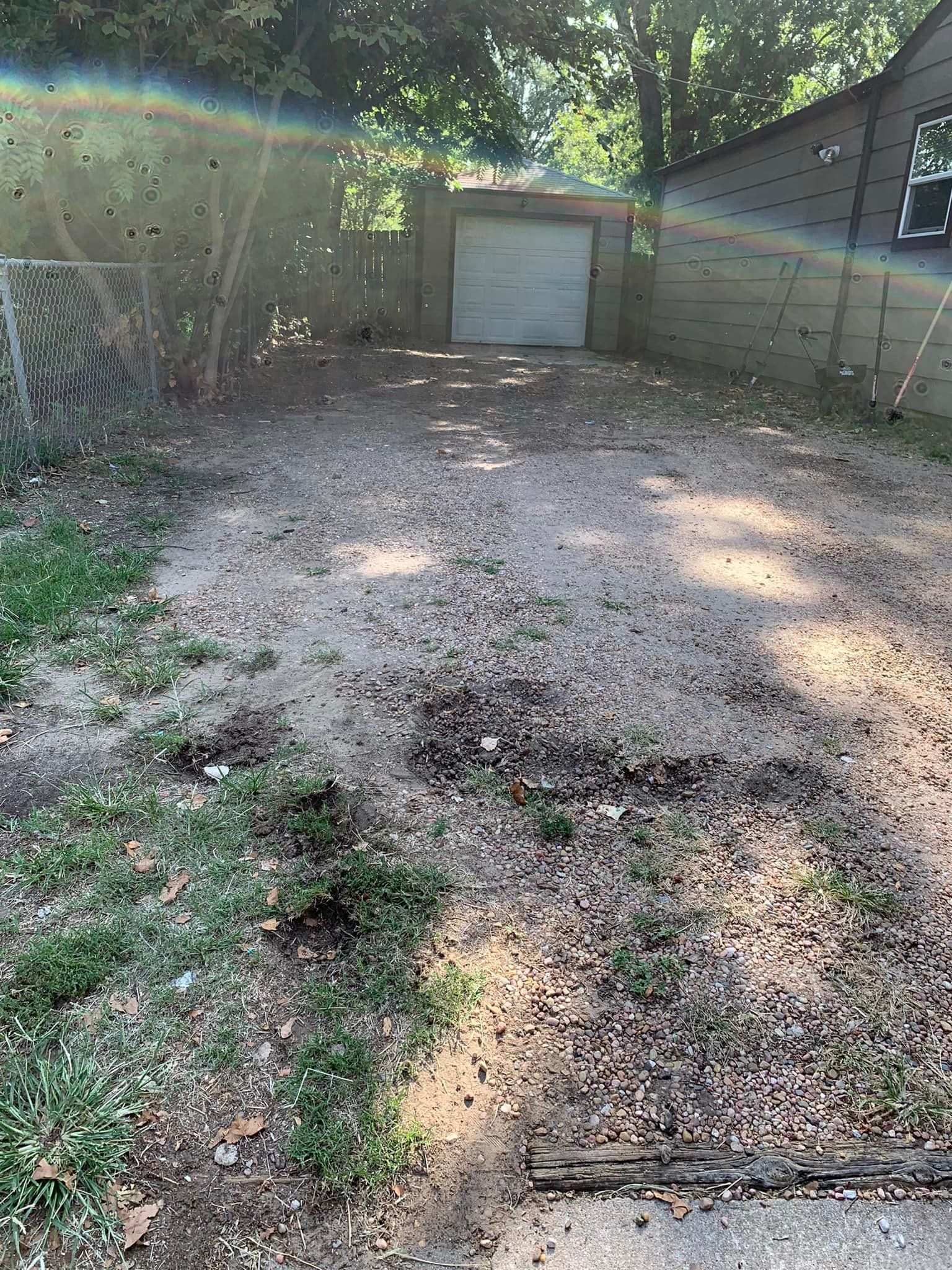 Gravel driveway leading to a garage, with a house on the right and a fence on the left.