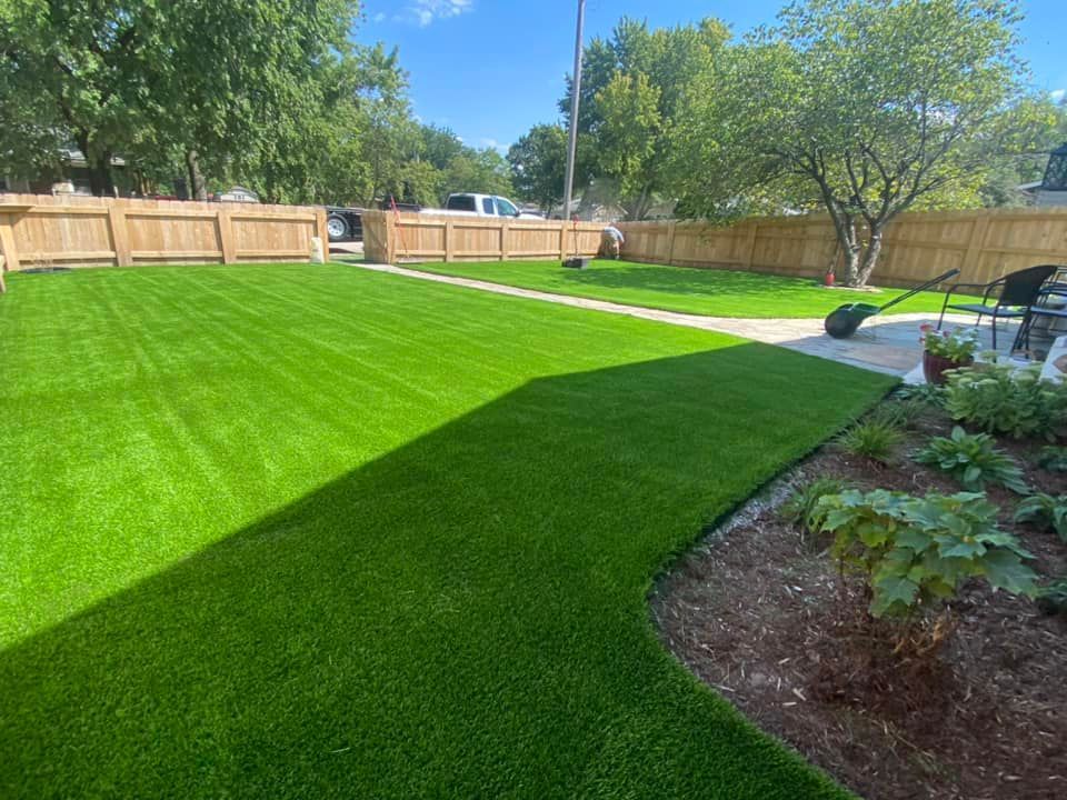 Lush green artificial turf backyard with wooden fence, pathway, and landscaping.