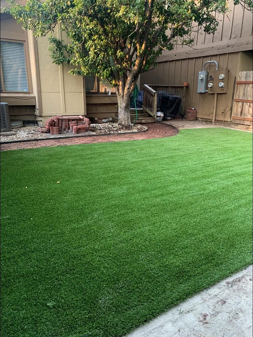 Green artificial turf yard with a brown fence and concrete patio.