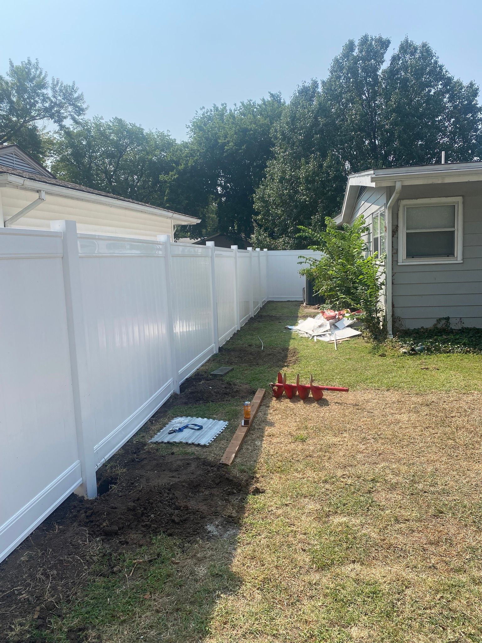 White vinyl fence alongside a house and a grassy yard on a sunny day.