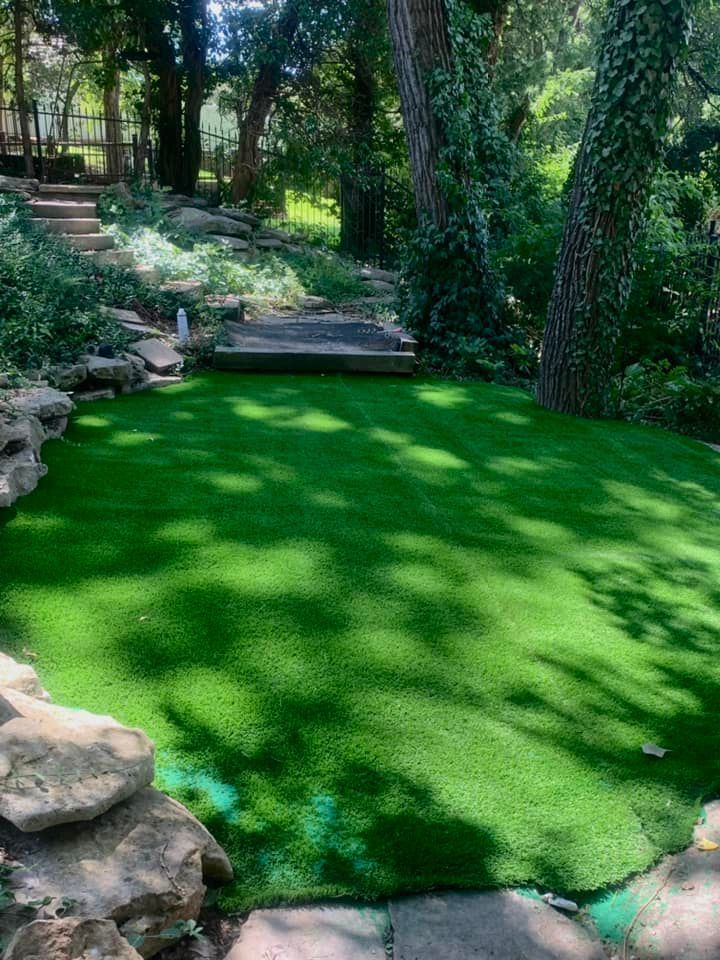 Green artificial turf area surrounded by rocks and trees, with stone steps leading upwards.