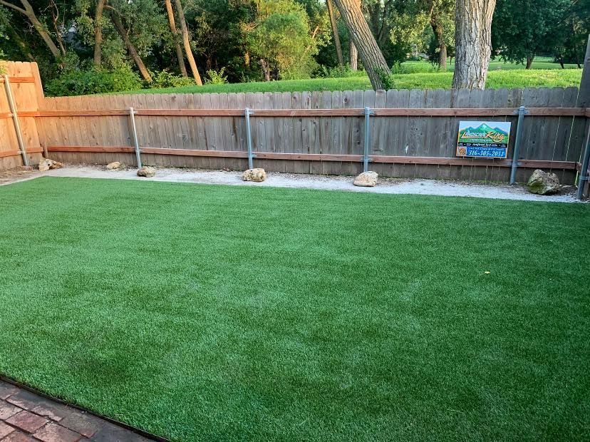 Green artificial lawn in a fenced backyard with a gravel border.