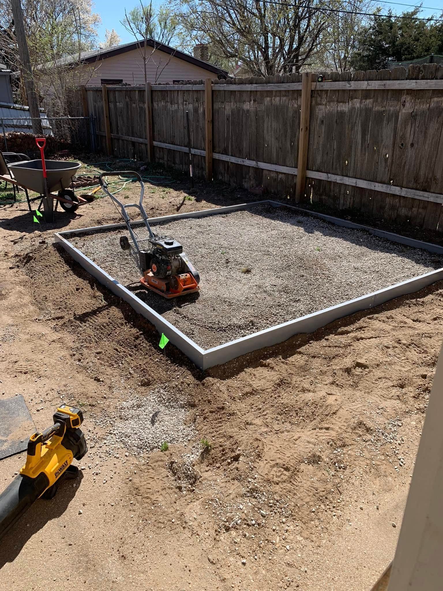 A gravel patio foundation in a backyard, being compacted by a machine.