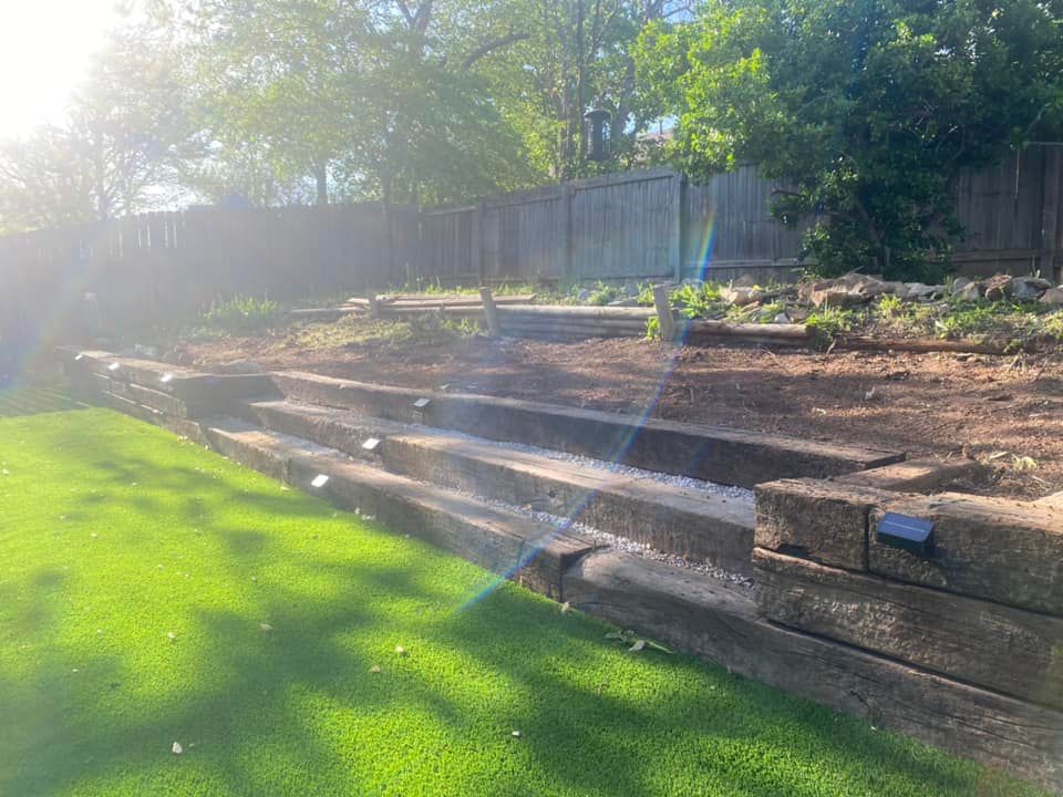 A sloped backyard with steps built from wood beams, with grass and a wooden fence.