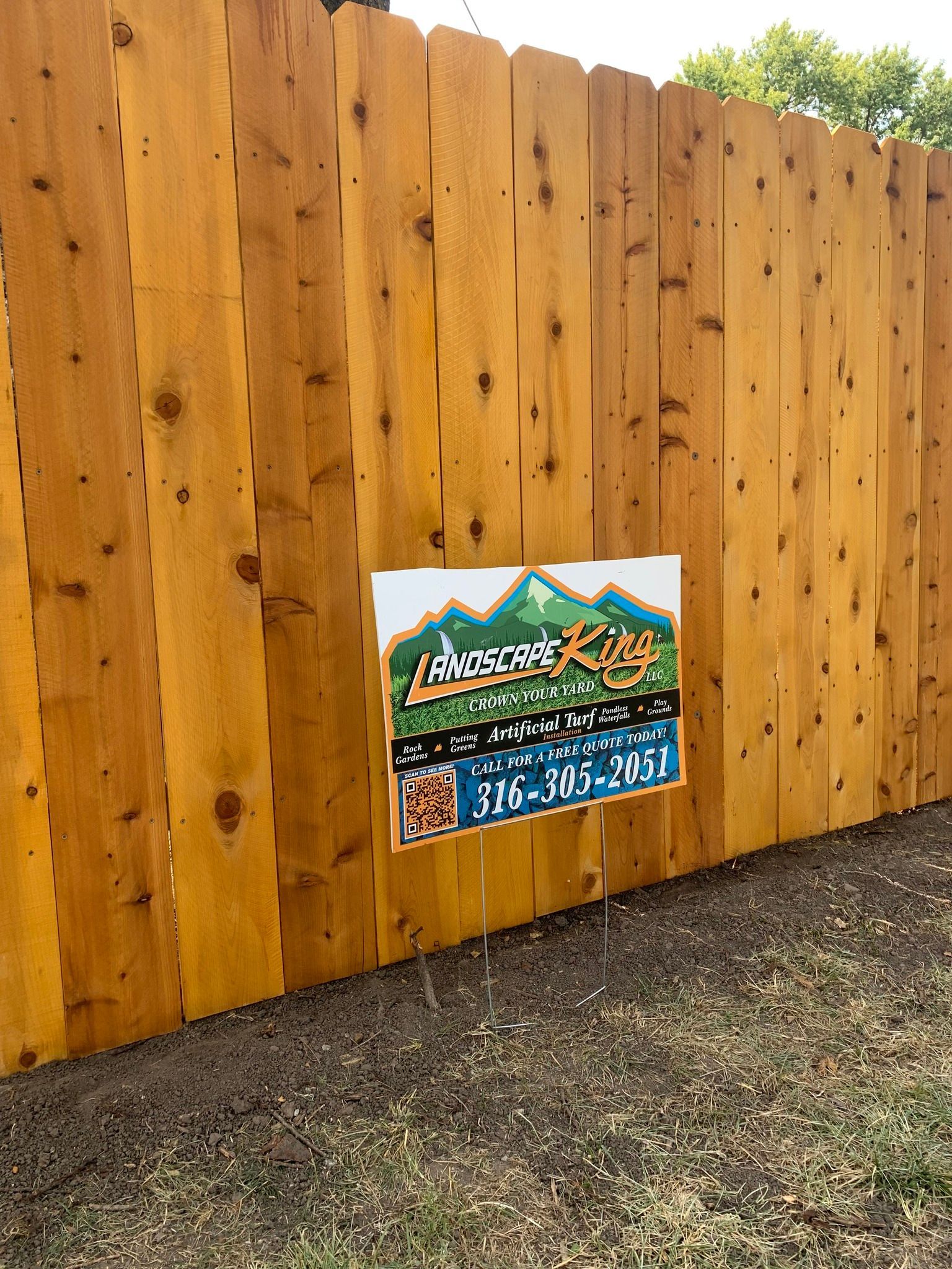Wooden fence with sign advertising landscaping services; phone number visible.