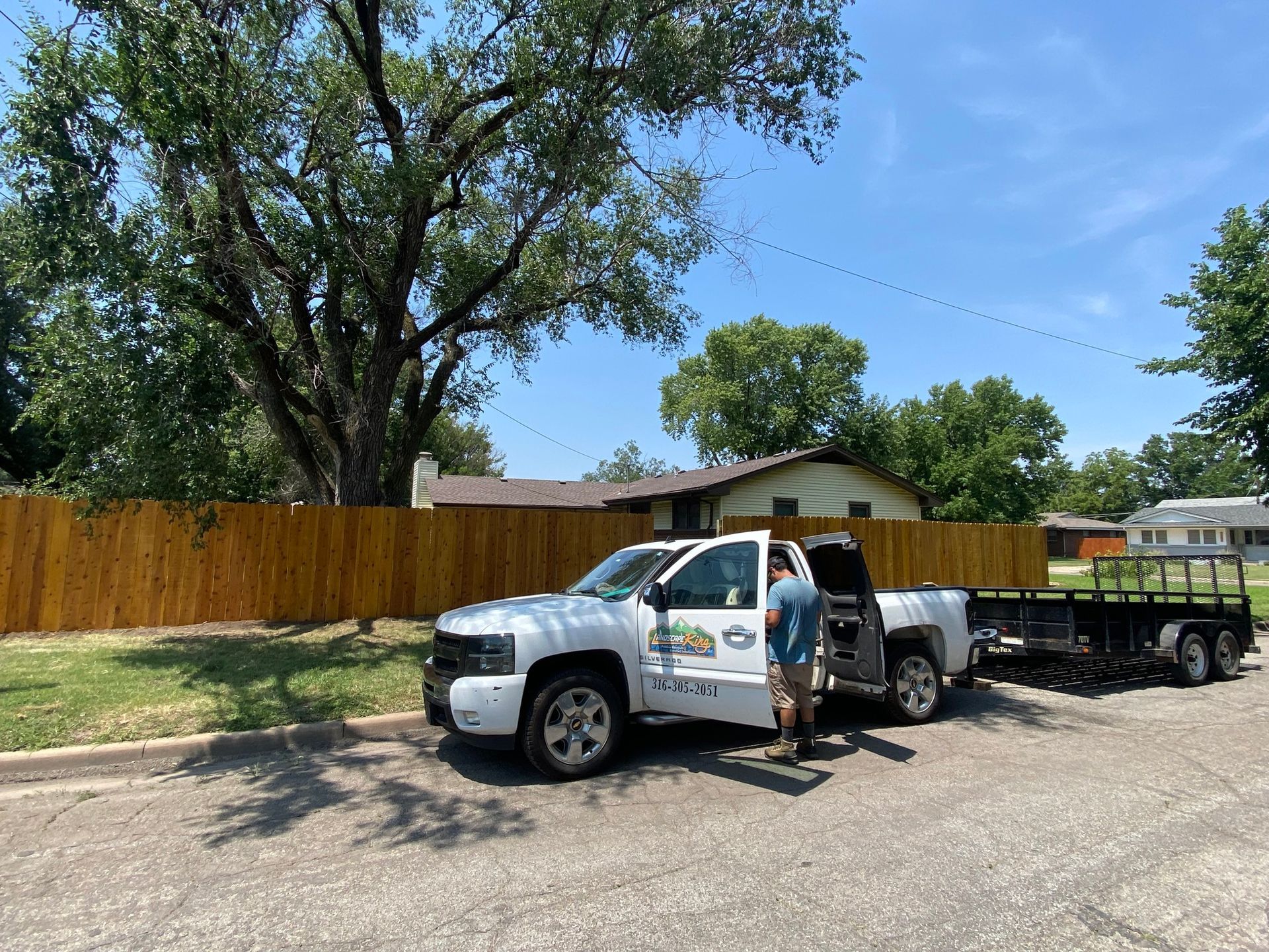 White pickup truck with trailer parked in front of a house, person standing beside the open truck door.