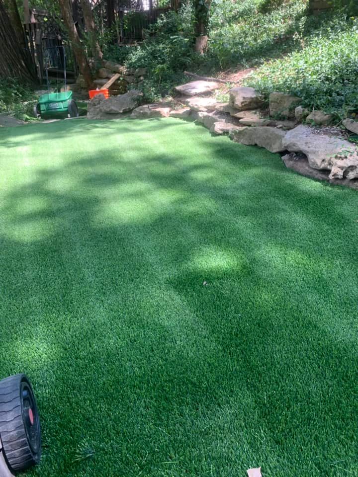 Green artificial turf lawn with rock border, partial view of a lawnmower.