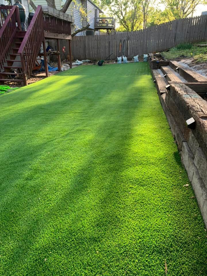 Green artificial turf lawn with a wooden fence and stairs in the background.