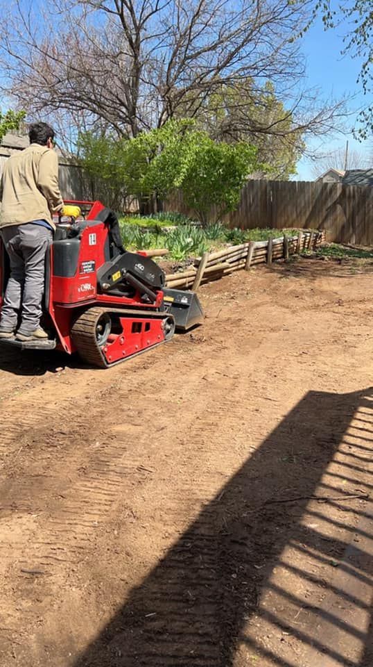 Man operating a red mini-excavator leveling dirt in a backyard, sunny day.