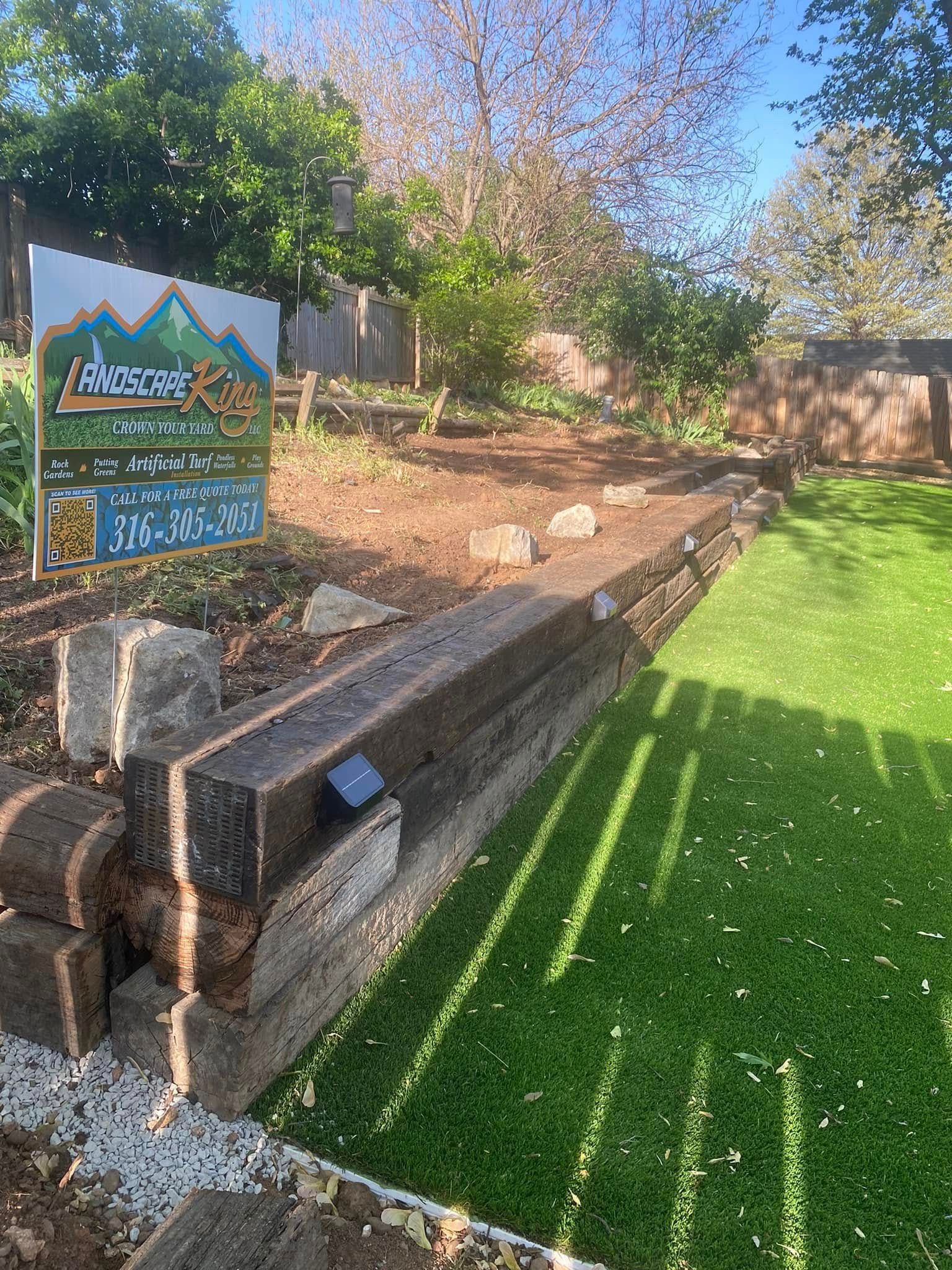 Wooden retaining wall next to artificial turf and a sign for a landscaping business.