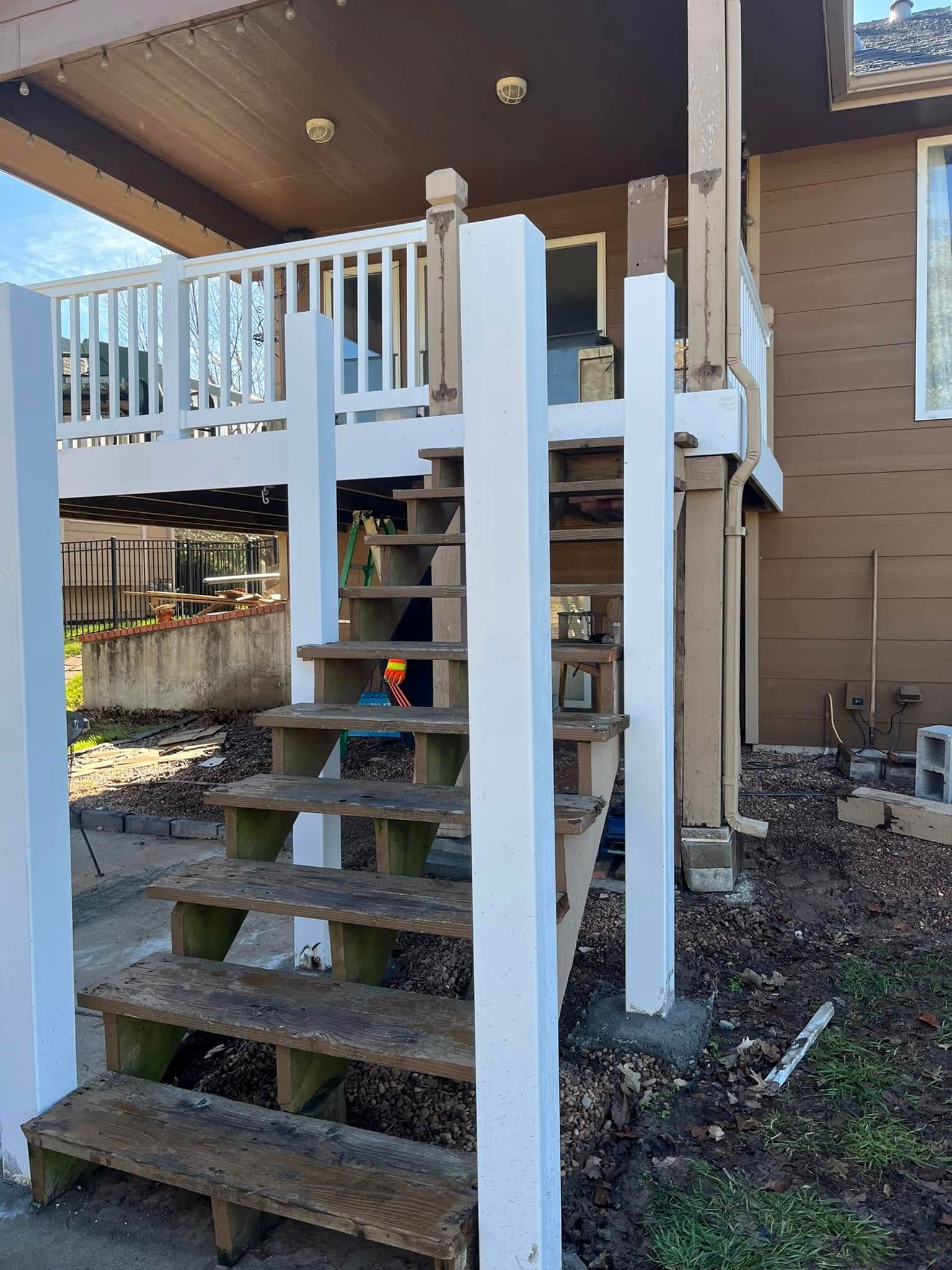 Wooden outdoor stairs leading up to a deck with white railing and support beams.