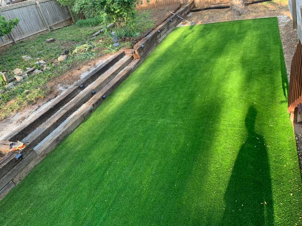 Artificial green grass lawn with wooden steps and retaining wall.