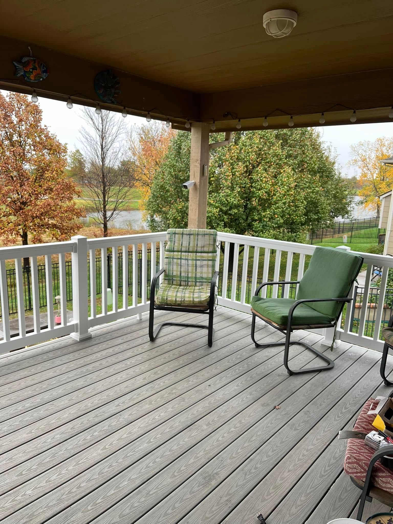Two chairs on a wooden deck, with a white railing and fall foliage in the background.